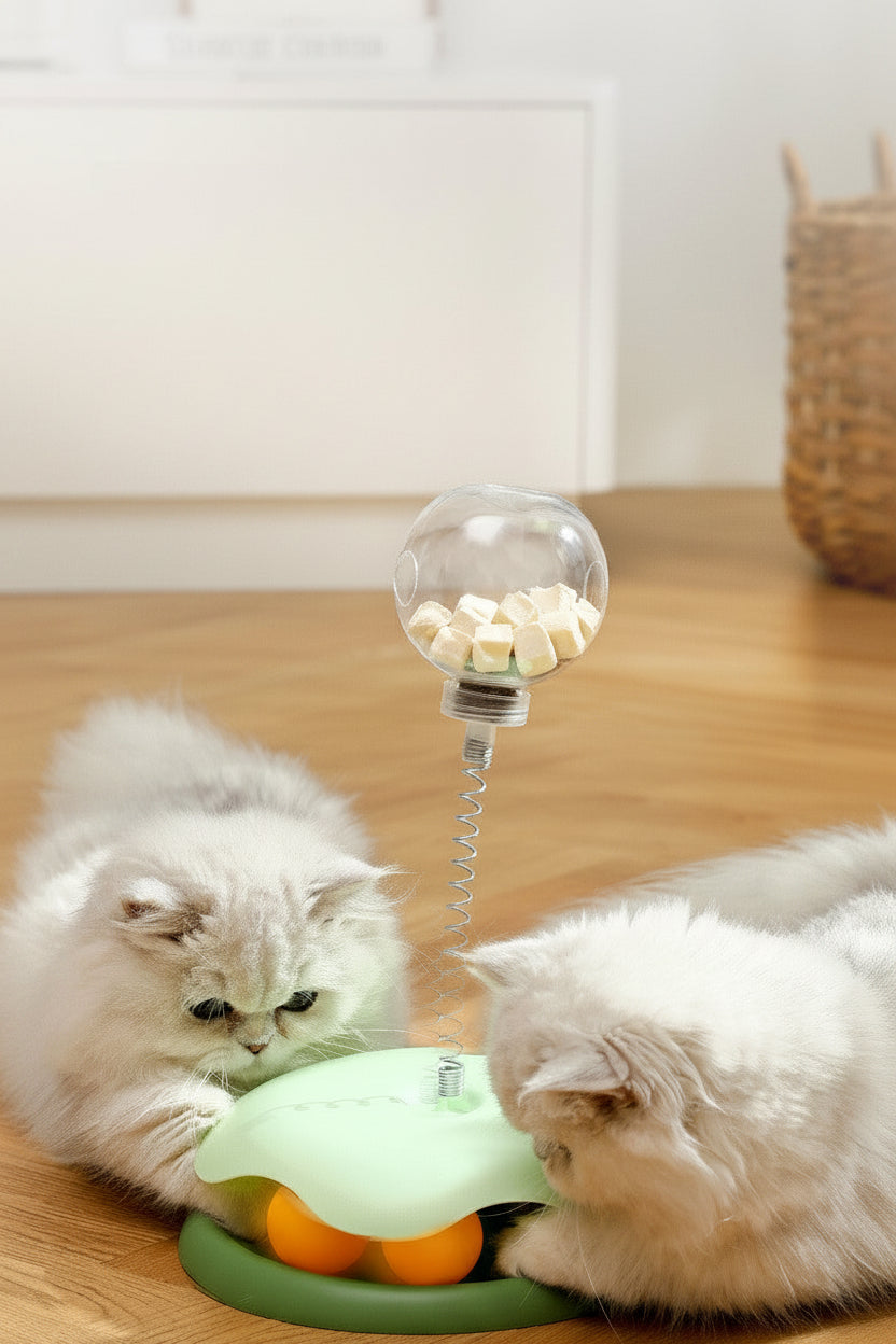 Two cats playing with a pet treat toy on a wooden floor.